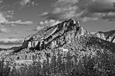 Tepesinde bir ev olan bir dağ. Ev uzakta ve dağ ağaçlarla kaplı.