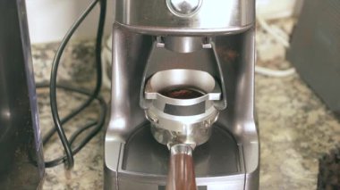 Elektrikli kahve öğütücüsünün portafilyuma taze fasulye serptiği ve mükemmel bir espresso hazırlarken yakın plan görüntüsü.