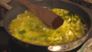 Doğranmış pırasa ve taze soğan, kaynayan zeytinyağında soteleniyor. Tahta spatula sebzeleri karıştırırken onlar da tavada pişiriyorlar.