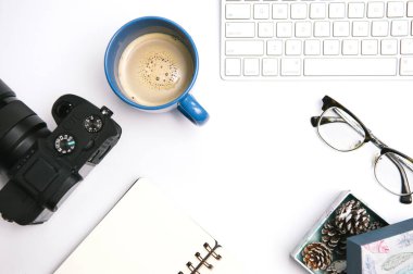 Tasarımcı ve fotoğrafçı çalışma alanı. Bir fincan kahve, defter, kamera ve bilgisayar klavyeli beyaz ofis masasının üst görünümü.