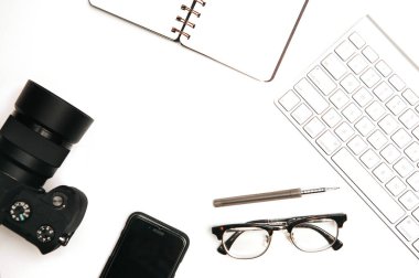 Tasarımcı ve fotoğrafçı çalışma alanı. Bir fincan kahve, defter, kamera ve bilgisayar klavyeli beyaz ofis masasının üst görünümü.