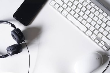 Akıllı telefonu, kulaklığı, bilgisayar klavyesi ve faresi olan beyaz ofis masası. Kopya alanı olan üst görünüm. Düz konum.