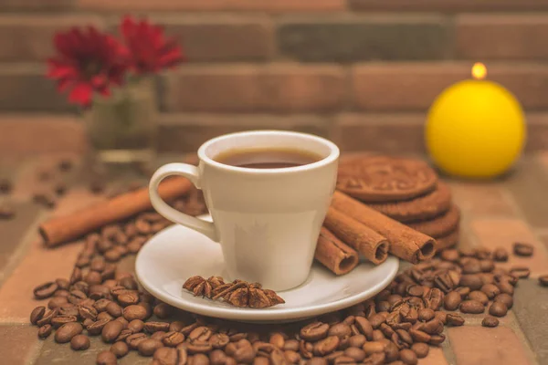 Bir fincan kahve, kahve çekirdekleri, kurabiyeler ve koyu arkaplanda bir mum.