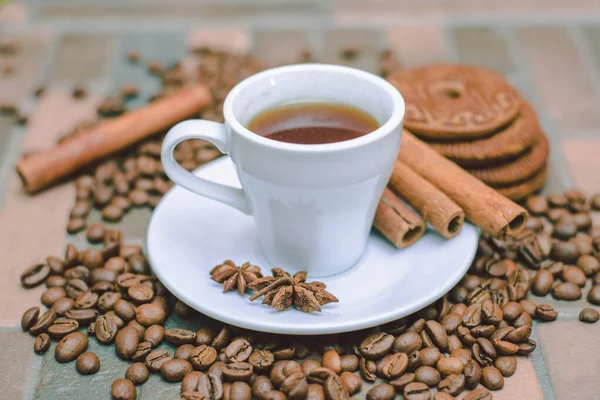 Bir fincan kahve, kahve çekirdekleri, kurabiyeler ve koyu arkaplanda bir mum.