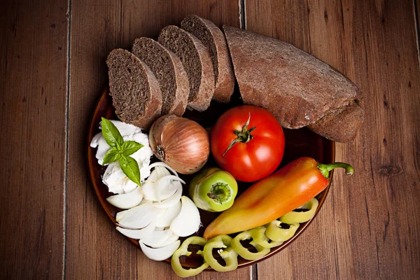 Pane e verdure fresche sul piatto isolato su dorso di legno — Foto Stock