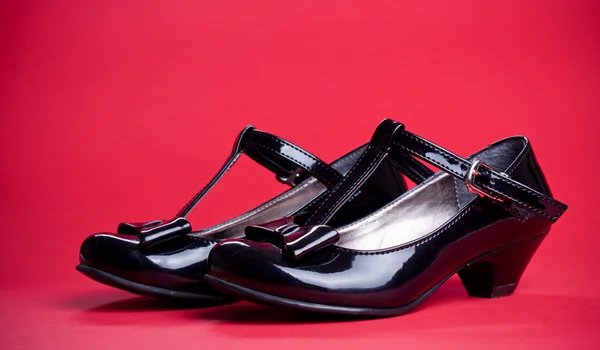 Black shine leather girl shoes with black ribbon isolated on red Stock Photo