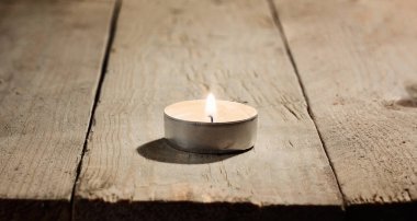 Lonely small lighted burning round candle on a wooden background of rough untreated pine boards. Macro photography with great depth of field clipart