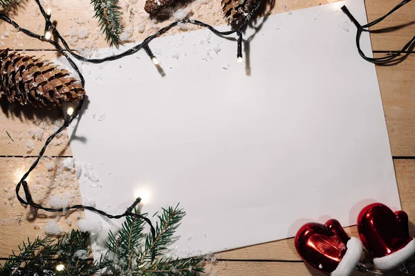 Karla kaplı tahta bir masanın arka planında süslü bacaklar, koniler ve bir çelenk ve tebrik etmek için beyaz bir kağıt ile süslenmiş. Noel ve Yeni Yıl kavramı