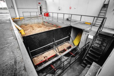 Katı yakıtlı endüstriyel kazanları vida çipli besleme sistemiyle ısıtmak için odun çipi deposu. Ahşap endüstrisinin atıklarıyla dolu beton bir tank..