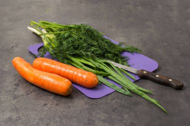 Kesme tahtasındaki dereotu ve soğan, bıçak. Taze bitkiler ve havuç..