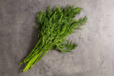 Koyu taşlı arka planda bir demet taze dereotu.