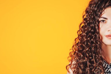 Sarı arka planda kameraya poz veren kıvırcık saçlı güzel bir kadın..