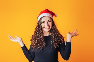 Siyah kazaklı güzel bir kadın ve sarı arka planda kırmızı bir Noel şapkası var..