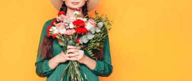 Sarı arka planda yeşil elbiseli büyük bir buket çiçek tutan bir kadın..