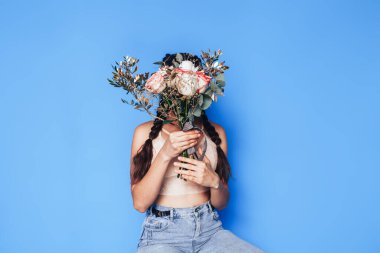 Küçük bir merdivende oturan ve elinde güzel bir buket beyaz gül tutan genç bir kadın mavi arka planda bahar zamanı.