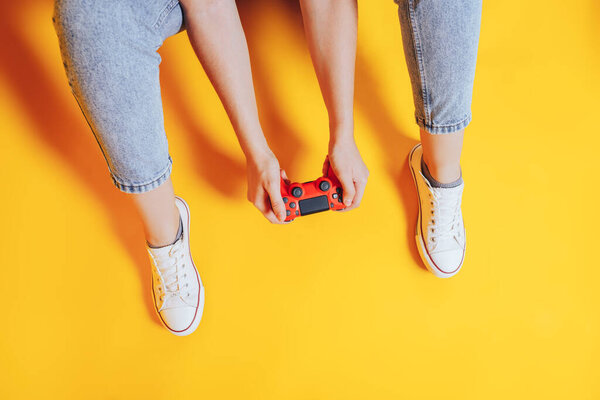 Woman sitting on a yellow background in white sneakers holding a gamepad.