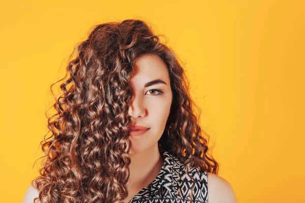 Beautiful woman with curly hair posing at camera on yellow background.