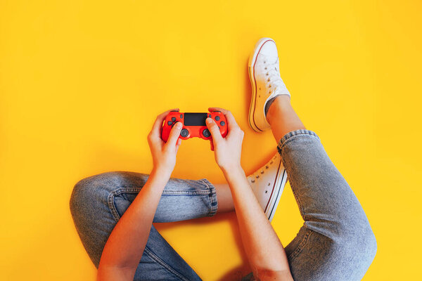 Woman holding gamepad in her hands in against of a yellow background. Promotion of women's esports. Advertising of esports equipment. Flat lay. Place for text.
