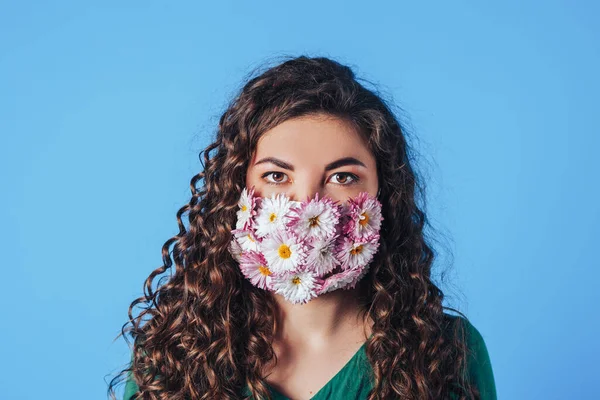 Young beautiful woman in protective mask made of blooming flowers on blue background. Breathe fresh air. Contaminated air