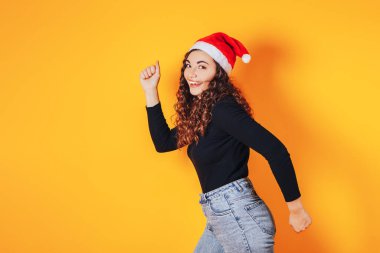 Sarı arka planda genç ve güzel bir kadın, kafasında Noel Baba şapkası var. Alışveriş yapan bir kadın. Noel havası. Metin için yer.