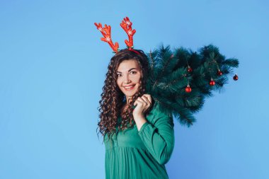 Sarı arka planda genç ve güzel bir kadının boynuzları var. Omzunda Noel ağacı tutan bir kadın. Noel havası. Metin için yer.