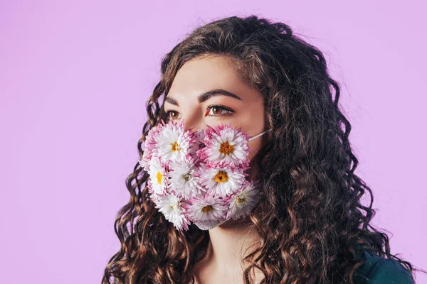 Young beautiful woman in protective mask of blooming flowers on pink background. Breathe fresh air. Contaminated air.