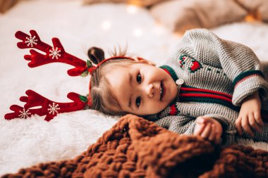 Küçük kız büyük bir yatakta yatıyor. Çocuğun boynuzları var. Noel havası.