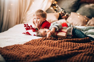 Erkek ve kız kardeş büyük bir yatakta birbirleriyle oynuyorlar. Noel havası. Kağıt ve düğümle sarılı bir hediye.