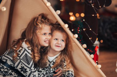 Çocuklar bir çadıra ve bir Noel geyiğine sarılarak oturdular. Noel havası. Tatili tüm ailenle kutla..
