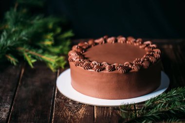 Beyaz tabakta çikolatalı pasta. Bir Noel ağacının arka planında. Tahta masa ve güzel bir desen. Doğum günü ve diğer tatiller için geleneksel tatlılar.
