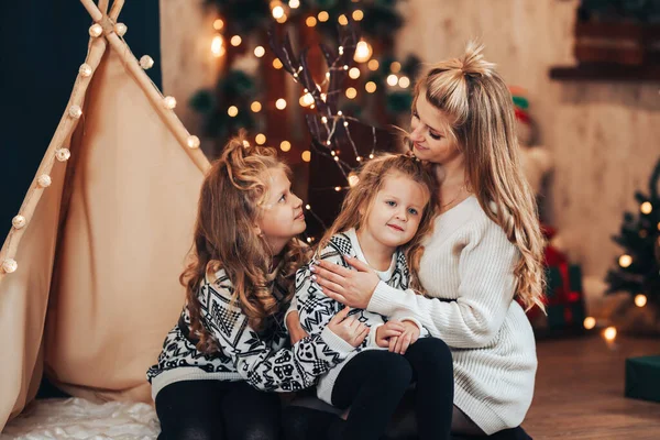 Children with mom sitting hugging on against a tent and a Christmas tree. Christmas mood. Celebrate the holiday with the whole family.