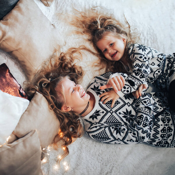 Children playing on a large bed. Friendly family concept. In the background there are lights from a garland.
