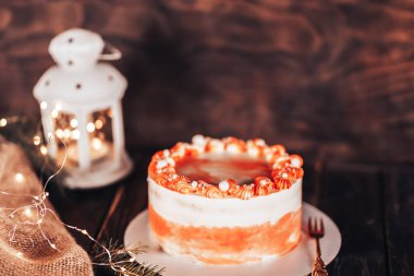 Beyaz bir tabakta çatallı kek. Her bayram için şeker. Tahta bir arka planda çelenkler ve bir fenerle.