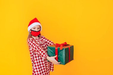 Hediyelerle dolu büyük kutuları tutan çocuk. Kafasında Noel Baba şapkası ve yüzünde tıbbi maske var. Noel havası. Bir salgın sırasında Noel reklamı için mükemmel bir fotoğraf.