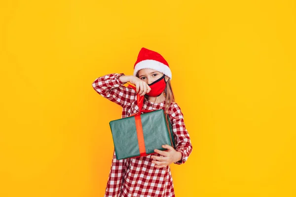 Hediyelerle dolu büyük kutuları tutan çocuk. Kafasında Noel Baba şapkası ve yüzünde tıbbi maske var. Noel havası. Bir salgın sırasında Noel reklamı için mükemmel bir fotoğraf. — Stok fotoğraf