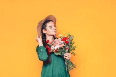 Sarı arka planda yeşil elbiseli büyük bir buket çiçek tutan bir kadın..