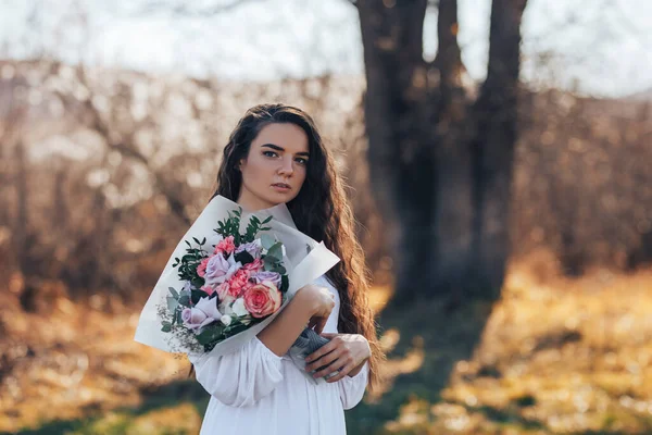 Młoda kobieta w białej sukience trzyma piękny bukiet róż — Zdjęcie stockowe