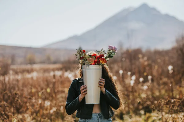 Doğada çiçeklerle dolu uzun demir bir kova tutan kadın. — Stok fotoğraf