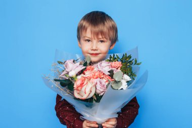 Küçük çocuk mavi arka planda elinde büyük bir buket gül tutuyor. Sevgililer Günü. Anneler Günü..