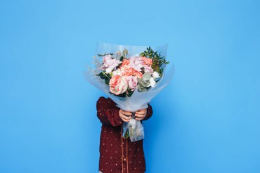 Küçük çocuk mavi arka planda elinde büyük bir buket gül tutuyor. Sevgililer Günü. Anneler Günü..