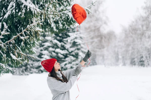 Woman with red heart-shaped balloons. Romantic mood on the background of a snowy park.