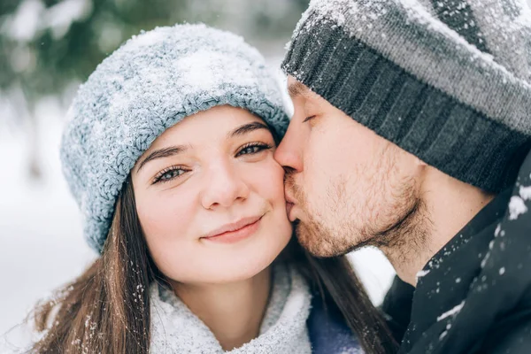 stock image Young couple in love in the park on a background of snow. A man kisses a woman on the cheek.