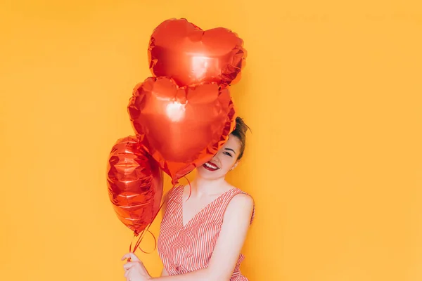 Sarı Arka Planda Elinde Kalp Şeklinde Balonlar Tutan Bir Kız — Stok fotoğraf