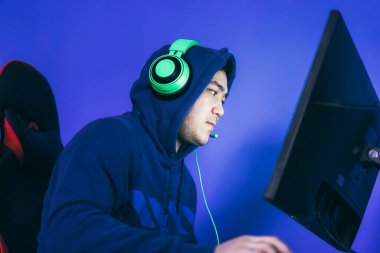 Oyuncu bir oyun sandalyesine oturur ve bilgisayar oyunları oynar. Oyuncunun kafasında yeşil kulaklık var..