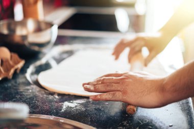 Adam evde, mutfakta pizza yapıyor. Mangırı oklavayla yuvarlar.