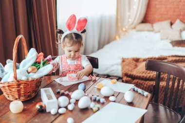 Paskalya için hazırlanan çocuk dini bayram için tahta masaya yumurta boyuyor. Tavşan kostümü giymiş kız..