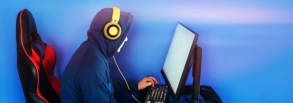 The gamer sits on a gaming chair and plays computer games. The player has yellow headphones on his head.