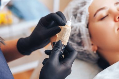 Kadın kalıcı makyaj için aletler hazırla. Sterilite için film bandı kullan, dövmeye hazır aletler kullan..