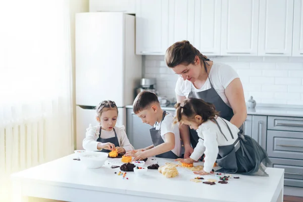 Mutter mit drei Kindern bereitet Plätzchen mit Süßigkeiten zu. Freizeitaktivitäten mit Kindern — Stockfoto