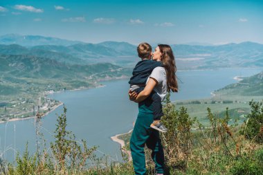Anne ve oğlu mavi denize ve dağlara karşı ayaktaydı.